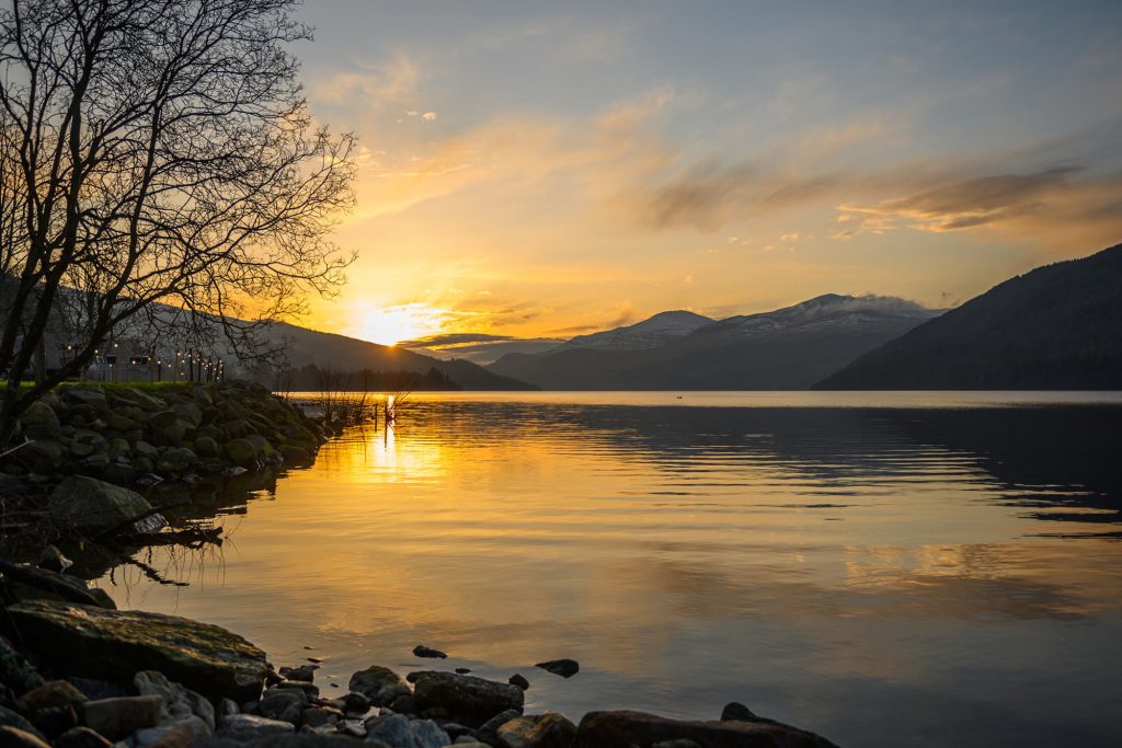 beautiful golden sunset reflected in loch tay rippling water surrounded by silhouetted hills