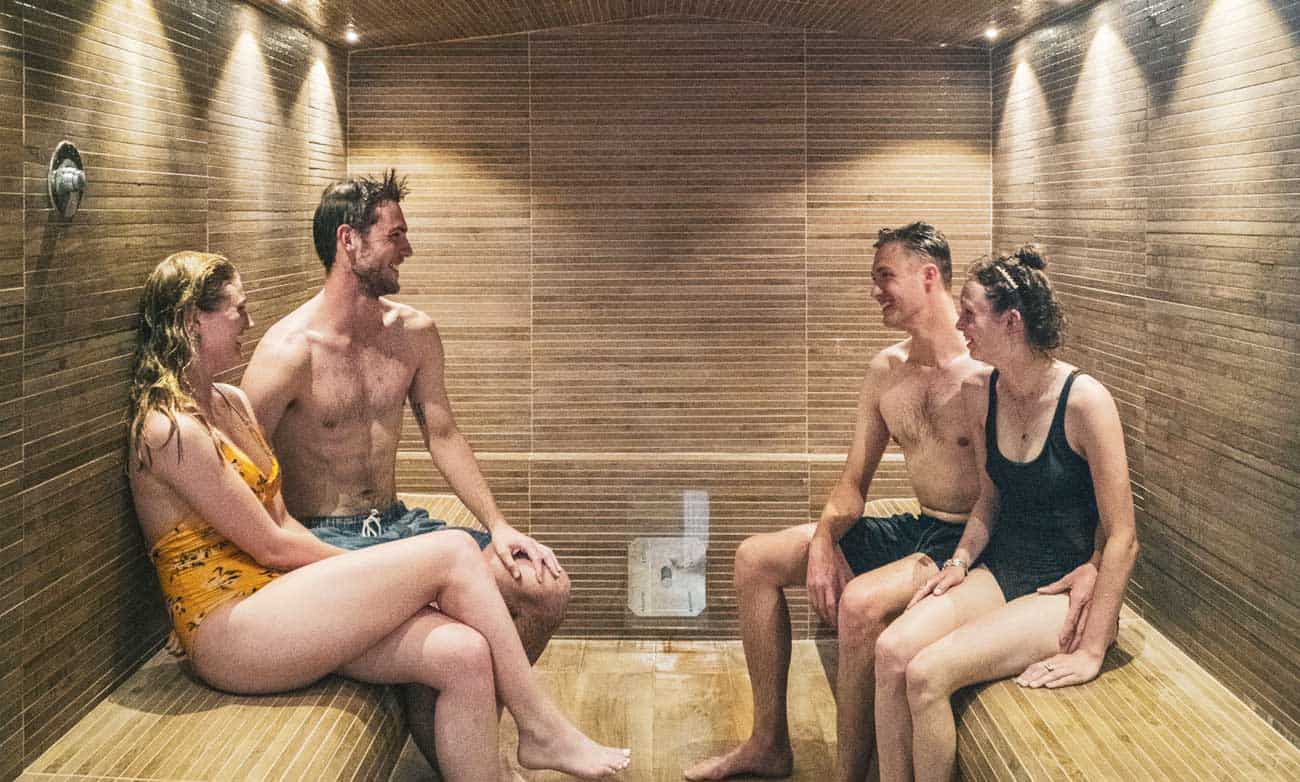 Four young people in bathing suits laughing and talking as the sit in Steam Room